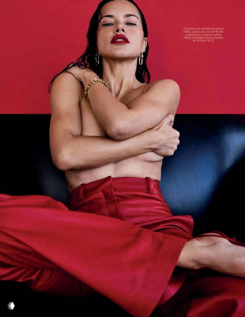 Интимный портрет: модель в красных шёлковых брюках сидит на диване, руки перекрывают грудь — эстетическая студийная фотосессия.