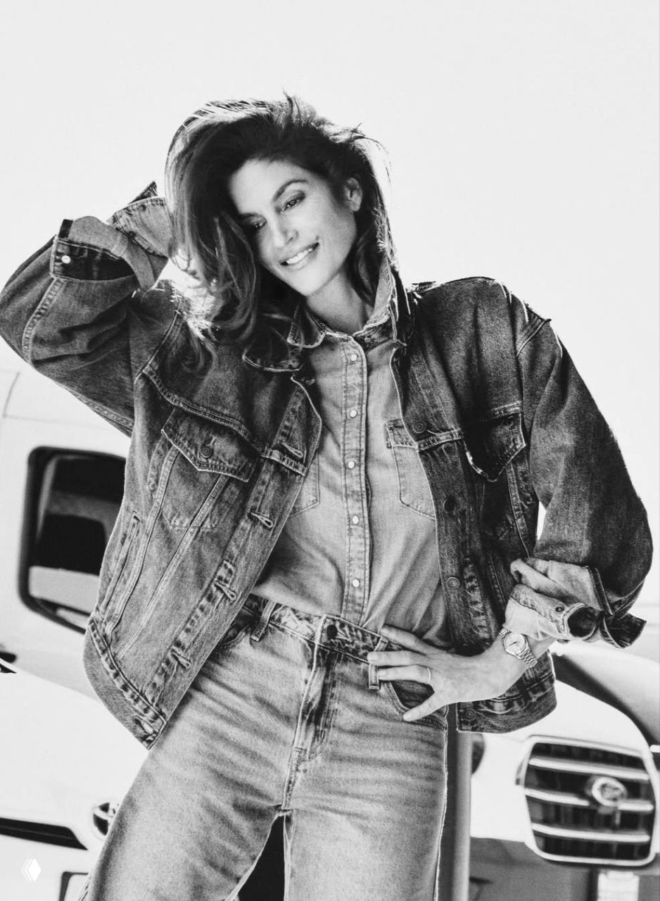 Чёрно‑белая студийная фотография: модель в джинсовой куртке и рубашке, руки на талии, классический fashion‑кадр.