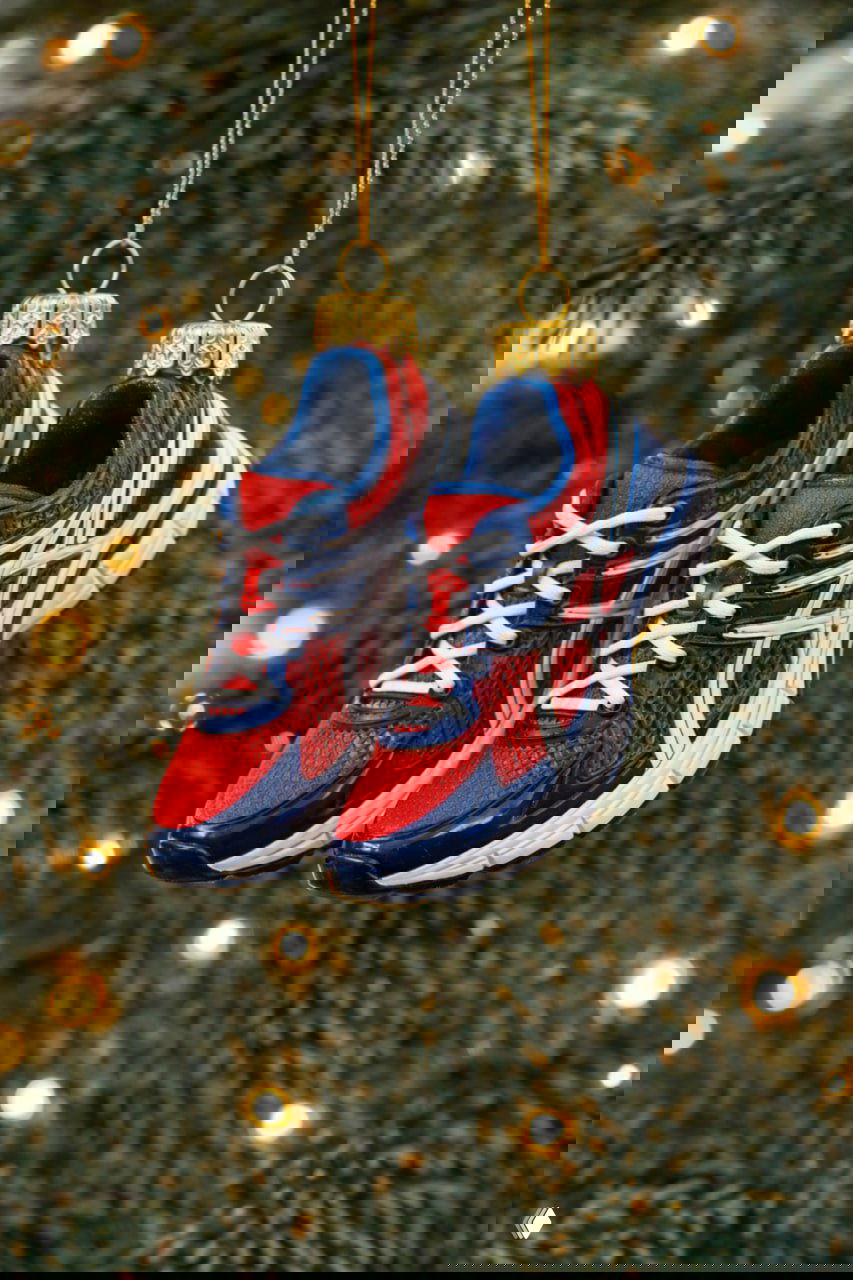 Пара миниатюрных кроссовок‑игрушек в красно‑синей гамме, подвешенная на ёлочной ветке — отсылка к забегам и активностям участников.