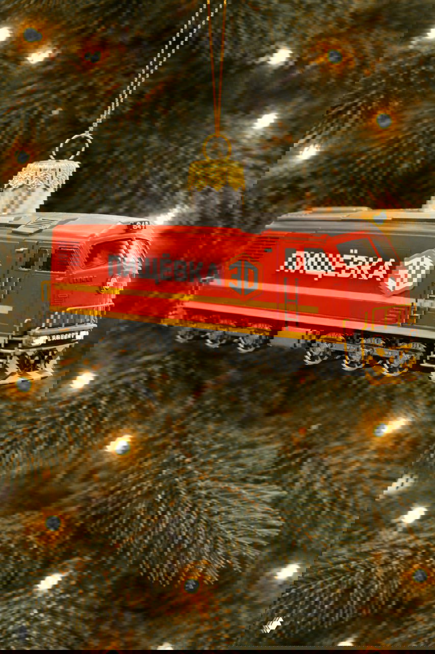 Красный локомотив‑игрушка с логотипом ПИЩЁВКА 3D на борту, подвешенный на ветке ели — символ роста, скорости и расширения географии проектов.