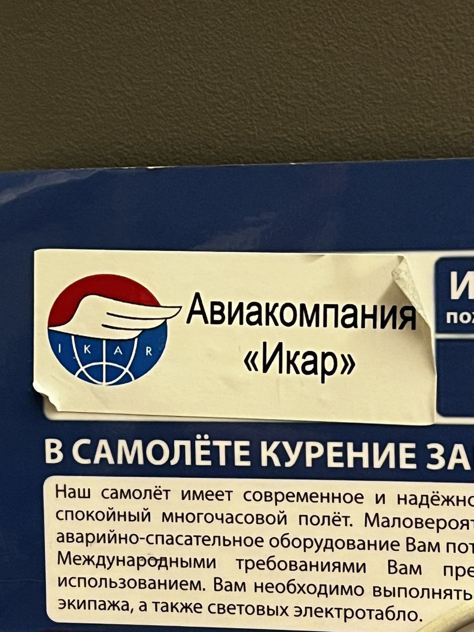 Фотография информационной таблички в салоне самолёта с логотипом «Икар» и фрагментом текста о запрете курения.