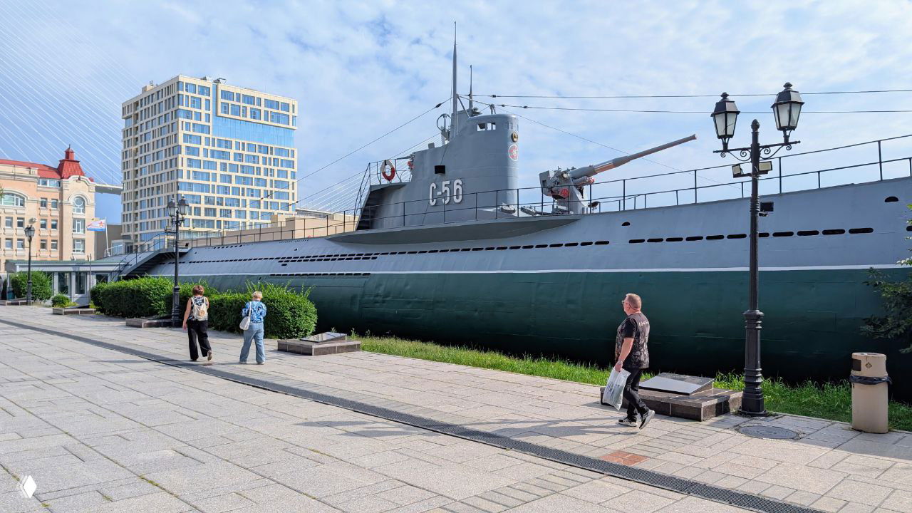 Вид на стоящую на набережной подводную лодку С-56 во Владивостоке — музейный корпус у Корабельной набережной, люди идут по променада.