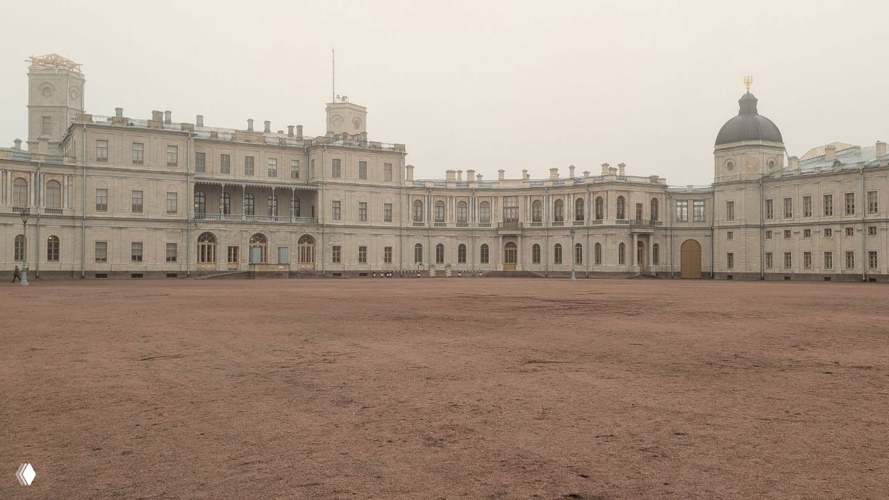 Пустой широкий двор Гатчинского дворца в тумане: бледные неоклассические фасады, низкая ноябрьская светимость и редкие посетители, почти пустая площадь.