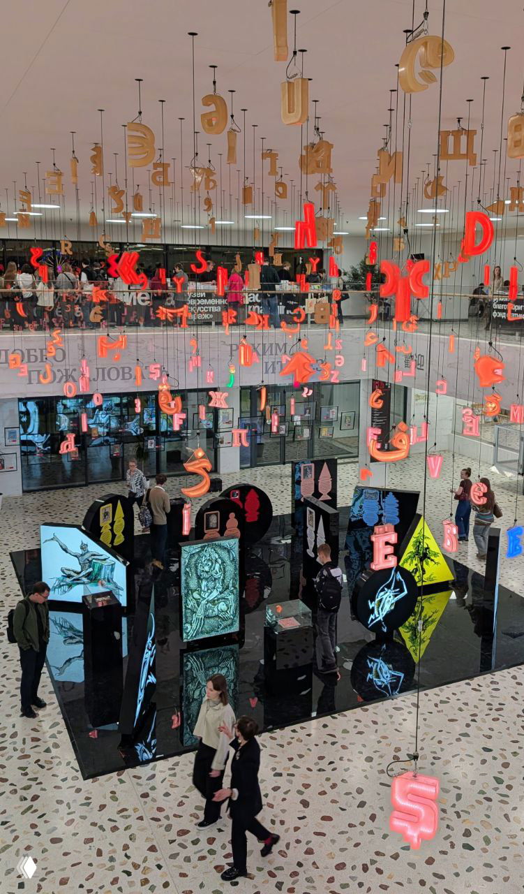 Внутренний вид холла крупным планом: инсталляция с висящими буквами разных алфавитов над выставочными экранами и посетителями.