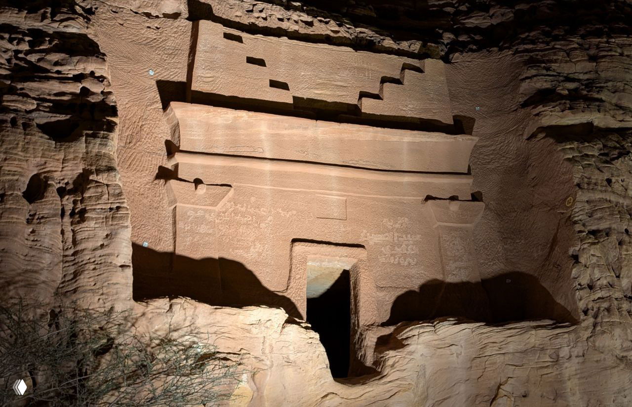 Крупный план входа в высеченную в скале гробницу: крепкие линии, ступенчатые элементы и текстуры песчаника при искусственном освещении.