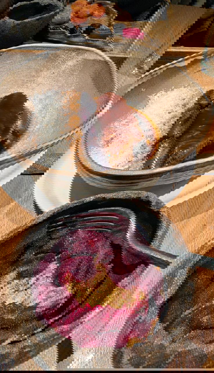 Керамическая подача: в большой миске тёмное мясное блюдо с соусом и стружкой, в маленькой — закуска, покрытая ломтиками свёклы и начинкой.