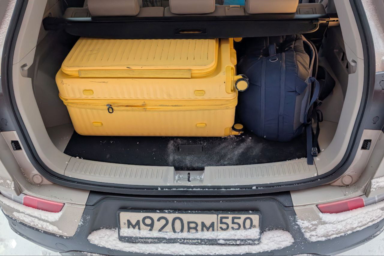 Багажник KGM Korando с жёлтым чемоданом и рюкзаком, видно пространство и относительно высокий пол багажного отделения, указывающее на запаску под фальшполом.