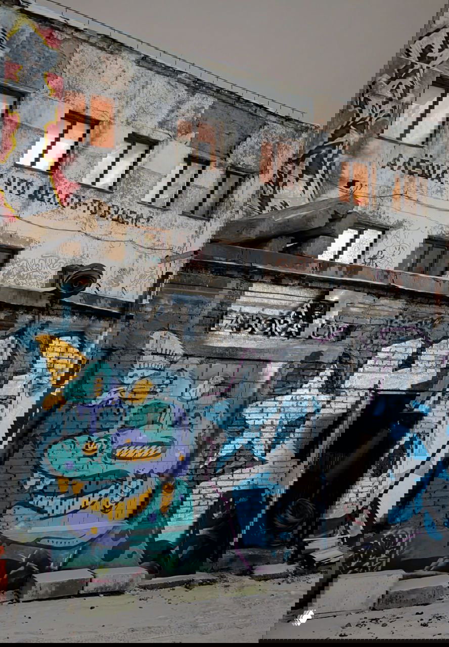 Фасад фабрики с цветным граффити и надписью «Алёша! Что делать-то будем?», открытая дверь и уличные художественные объекты в снегу.