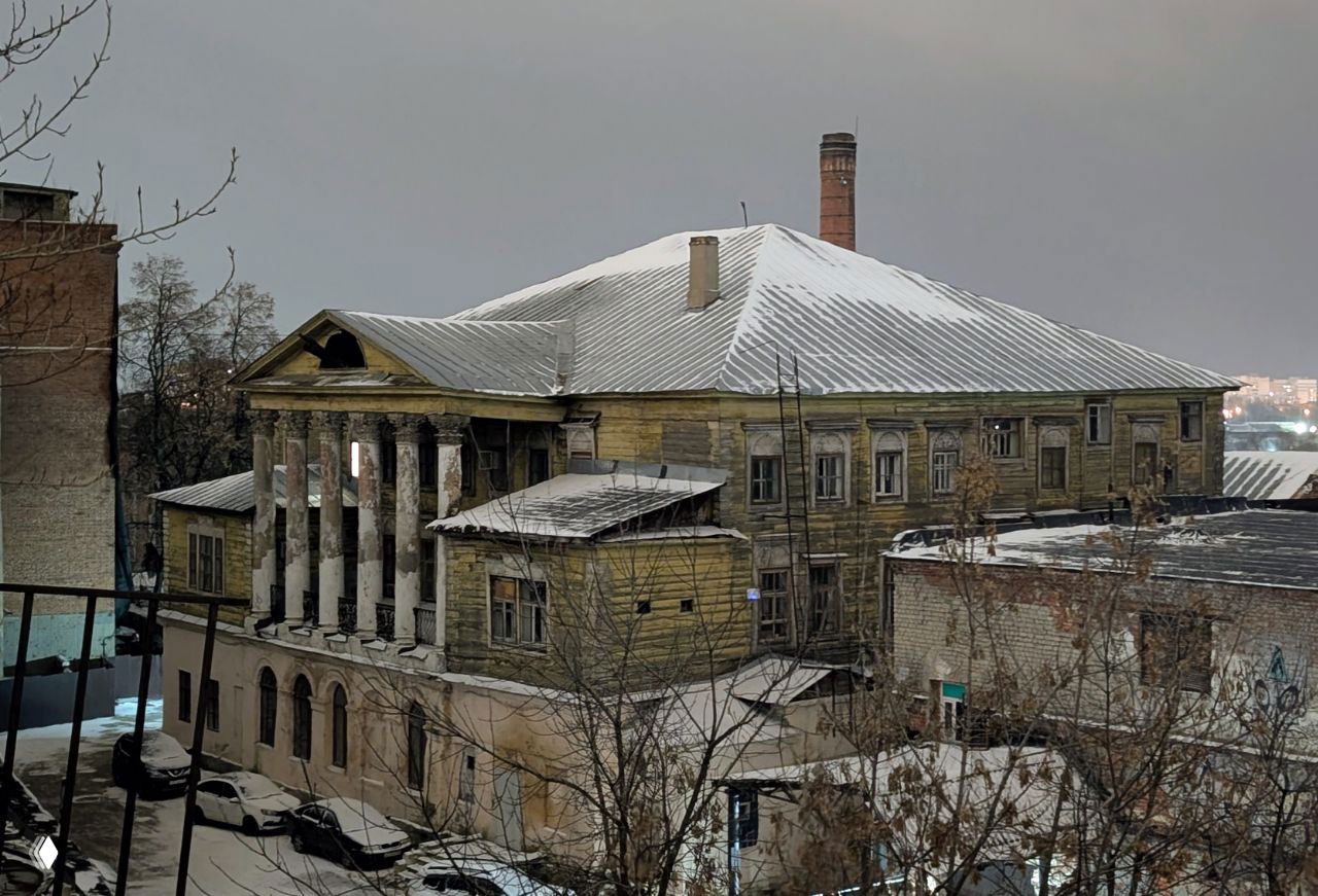 Вид на внушительное старое здание фабрики с колоннадой и дымоходом, покрытое снегом — архитектура и спад империи Алафузова.