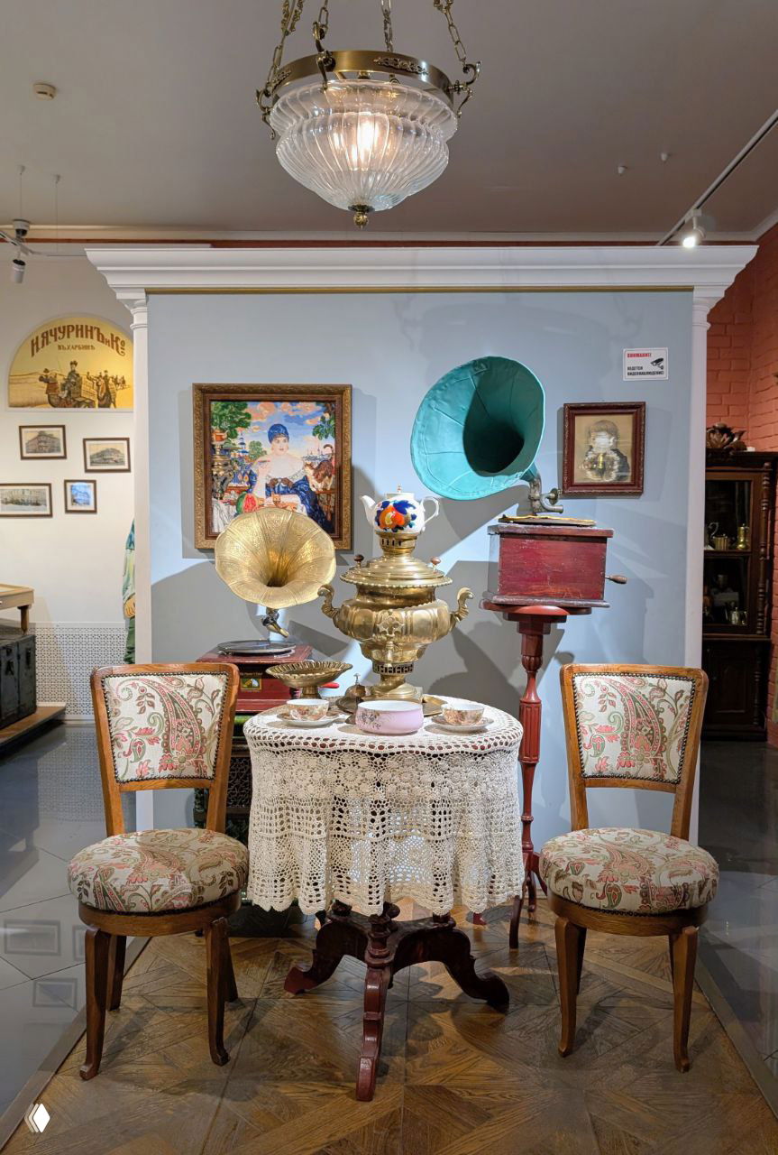 Интерьерный фрагмент экспозиции Музея чая: столик с антикварным самоваром, граммофоны и стулья, оформленные в стиле купеческой гостиной
