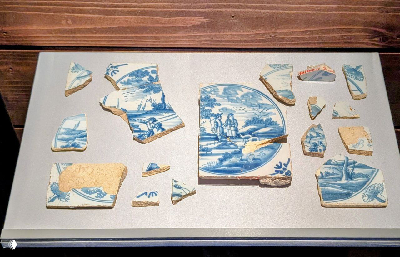 Фрагменты керамики с голубой росписью разложены на подиуме — обломки посуды и декоративных элементов в музее.