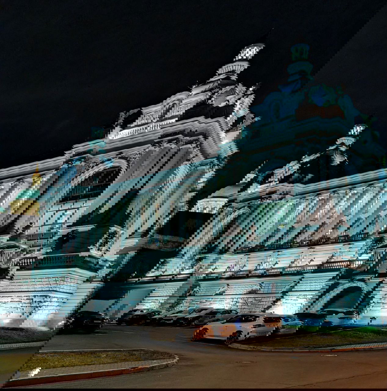 Общий вид корпуса Дворца земледельцев в Казани в ночном свете, показаны колоннада, купола и парковка у здания.