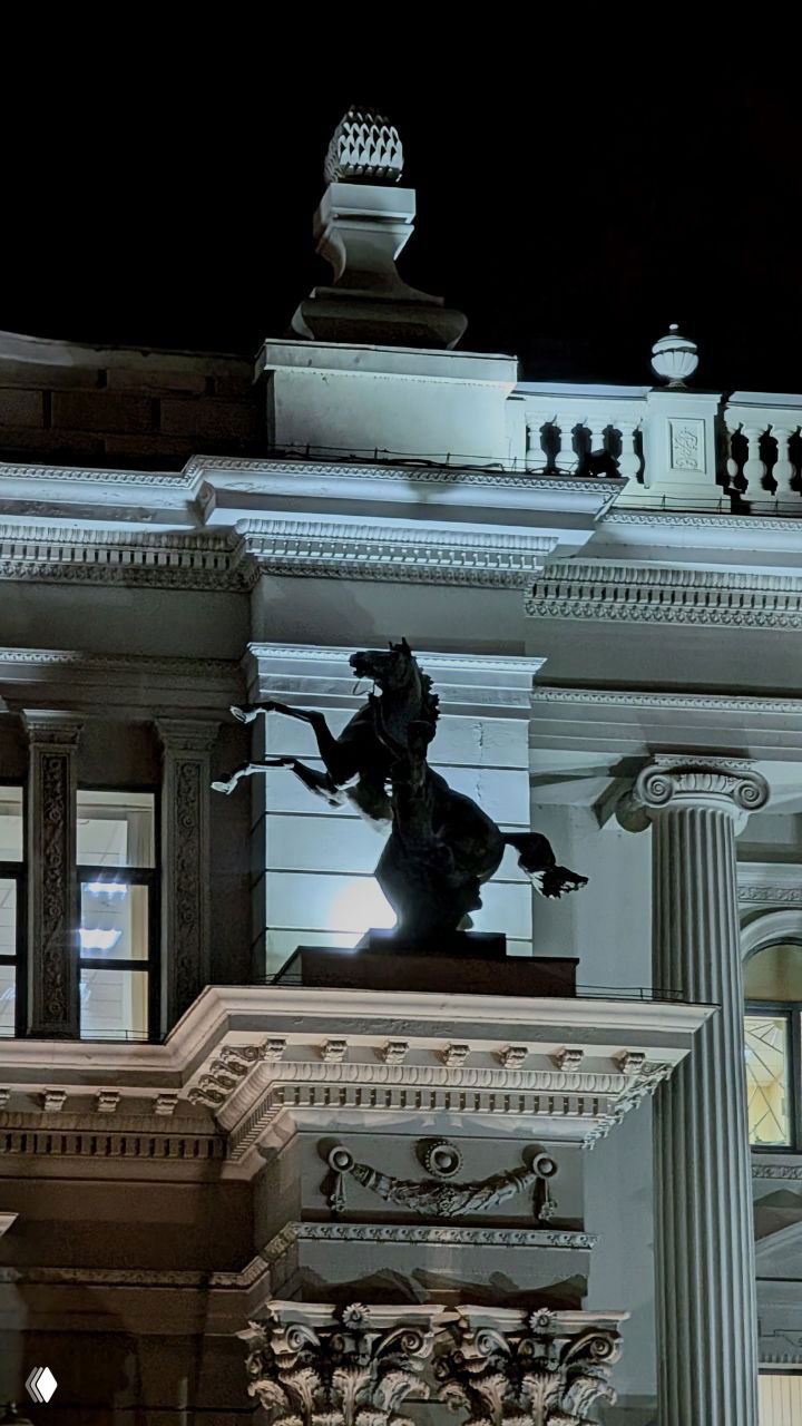 Скульптура скачущего коня на угловом фоне фасада Дворца земледельцев; вид подчёркивает монументальные элементы декора.
