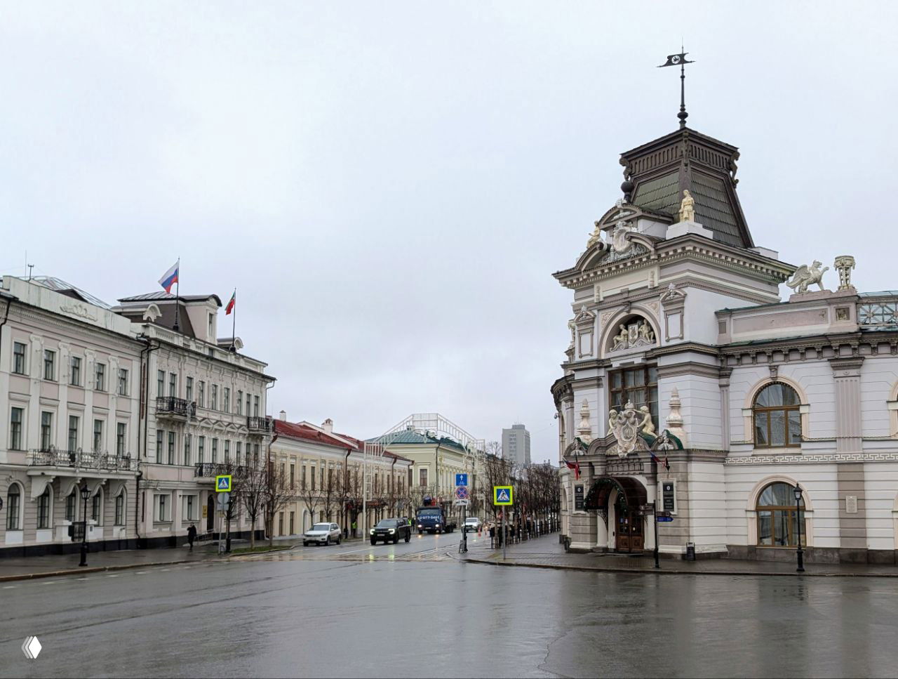 Исторические здания в центре Казани, архитектура с европейскими мотивами и правительственные флаги на фасадах в дождливый день.