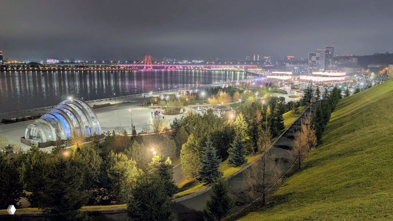 Ночной вид на набережную с подсветкой, прогулочные зоны и мосты через реку — сцена городской жизни и вечерних развлечений.