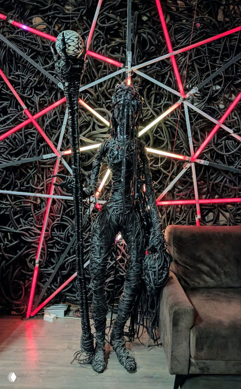 Современная инсталляция — фигура, собранная из кабелей с неоновыми элементами на фоне тёмной стены, арт-объект в городской галерее.