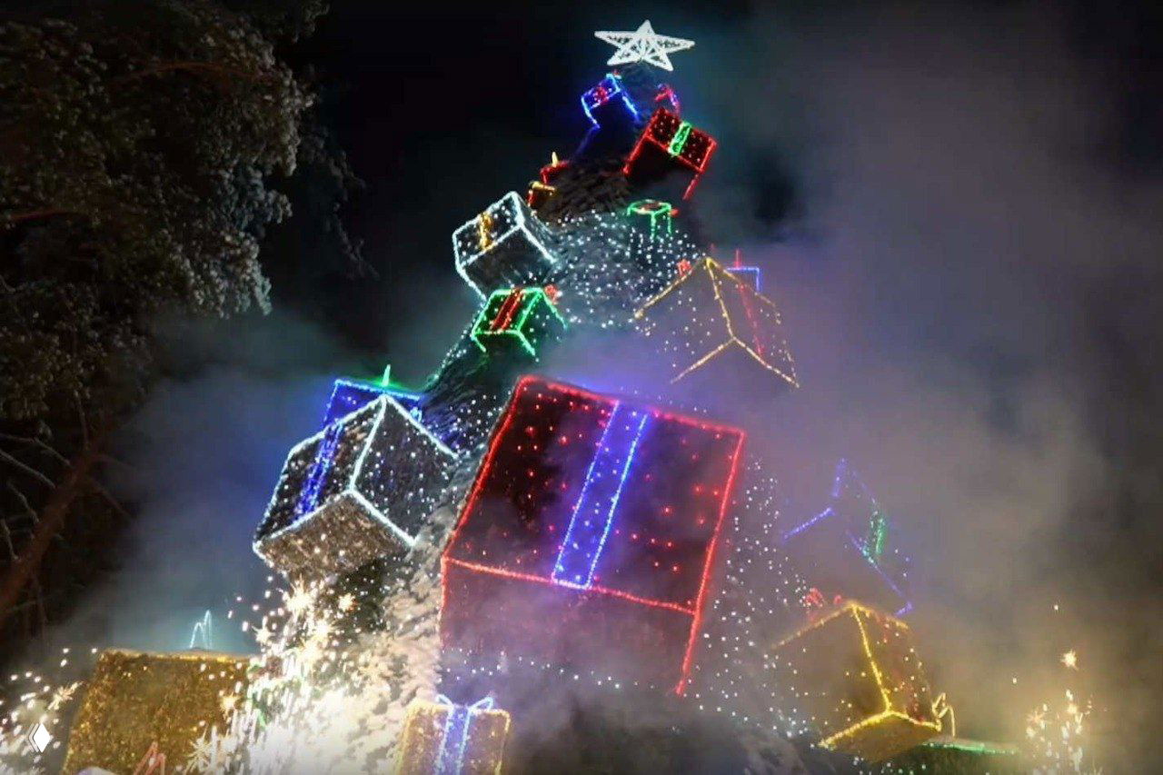Новогодняя ёлка в Великом Устюге украшена подсвеченными подарочными коробками и гирляндами, вокруг видны эффекты и дым от салюта.