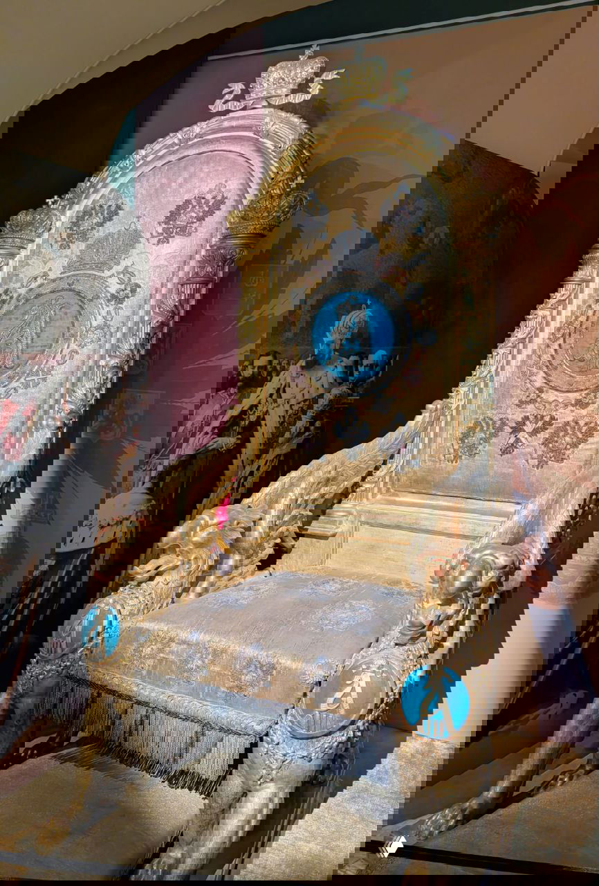 Золочёное коронационное кресло с грифонами-подлокотниками и синими медальонами, крупный план экспоната в музее Гатчины при драматичном свете