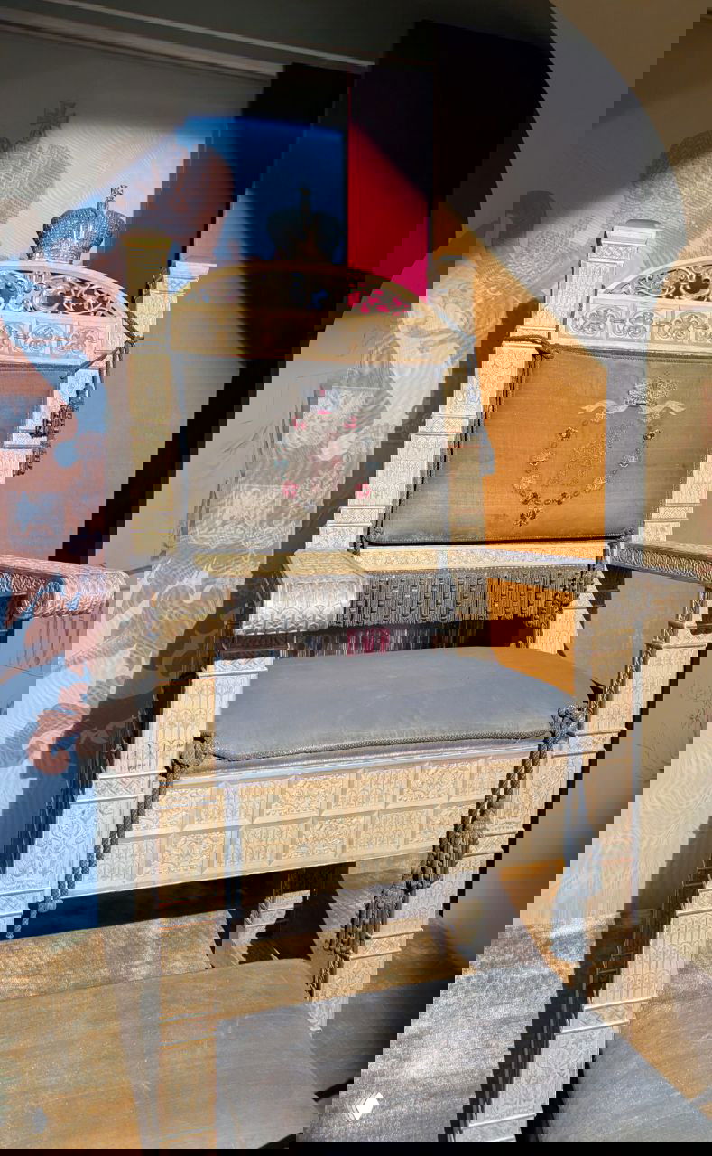 Прямоугольное деревянное кресло с тёмной обивкой и резной спинкой, вид экспоната с подставкой для ног под боковым светом в музее