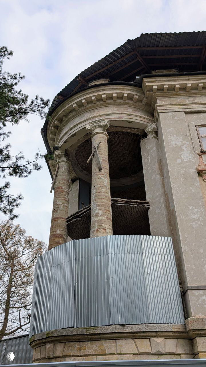 Угловая часть бельведера с колоннадой и временным ограждением из профлиста; вид снизу подчёркивает разрушение внутренних перекрытий.