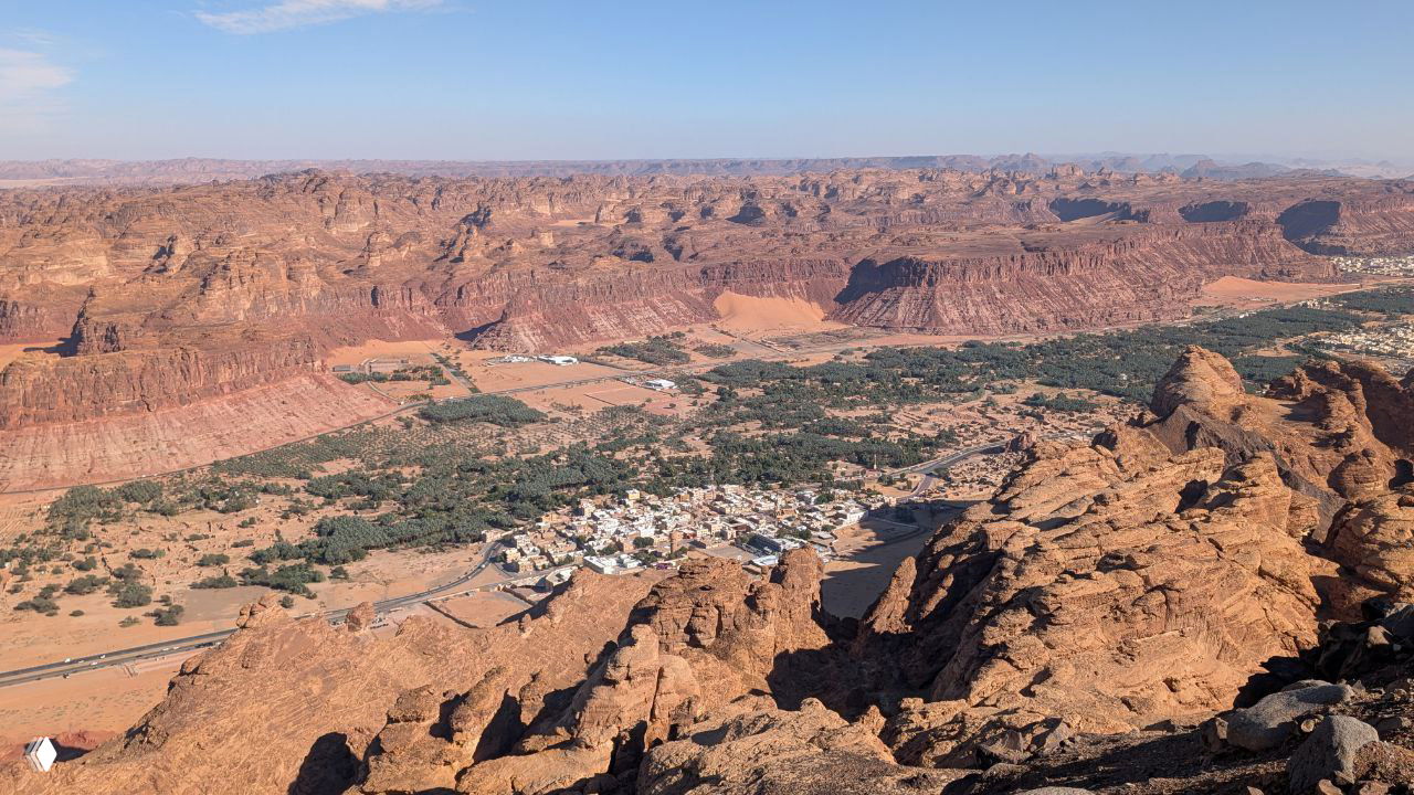 Панорамный вид с утёса на красные скалы и оазис в долине с разбросанными домами — характерный пустынный каньонный ландшафт.