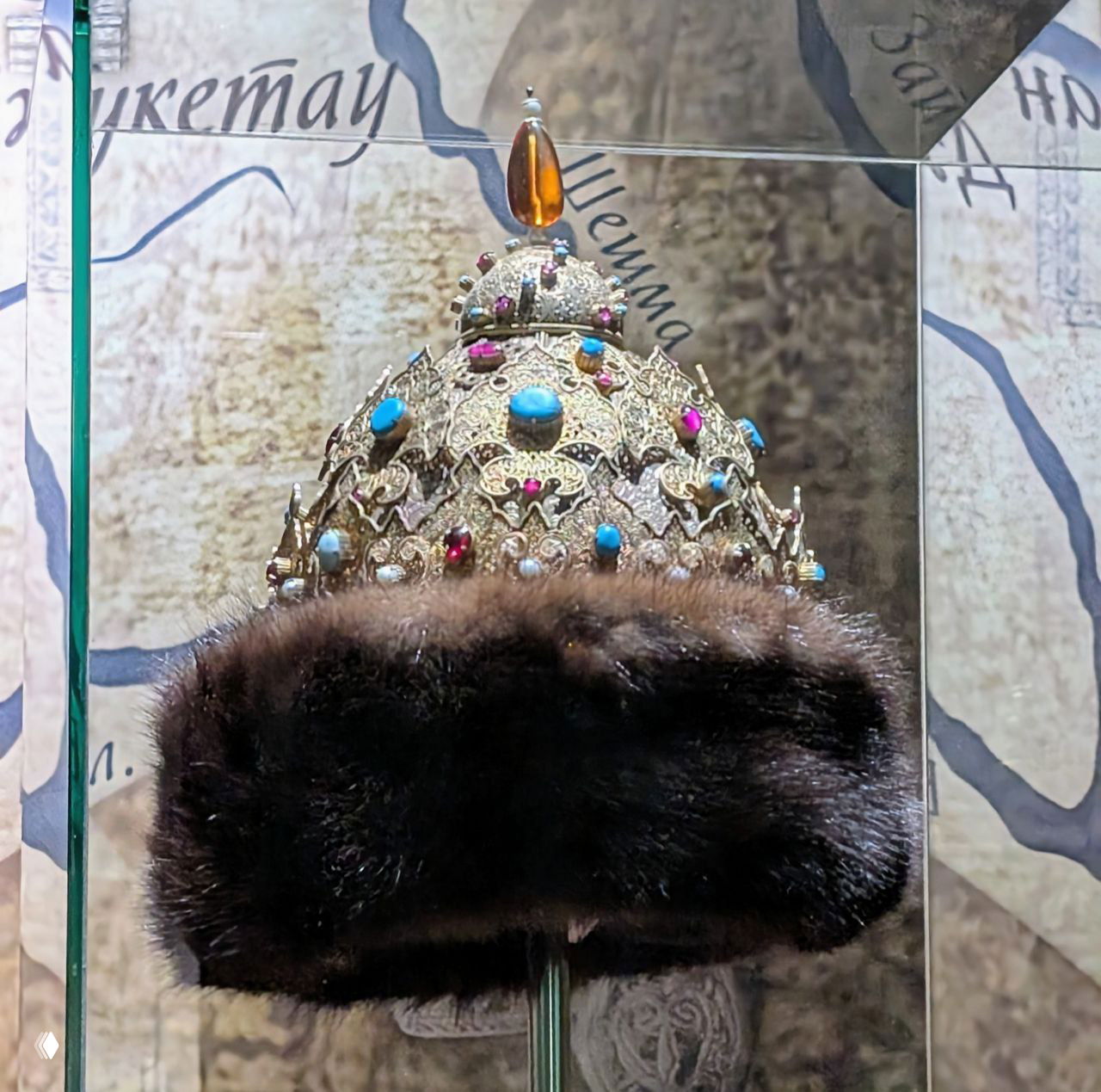 Богато украшенная корона с бирюзой и драгоценными вставками на подставке в стеклянной витрине — предмет роскоши из собрания музея Казани.