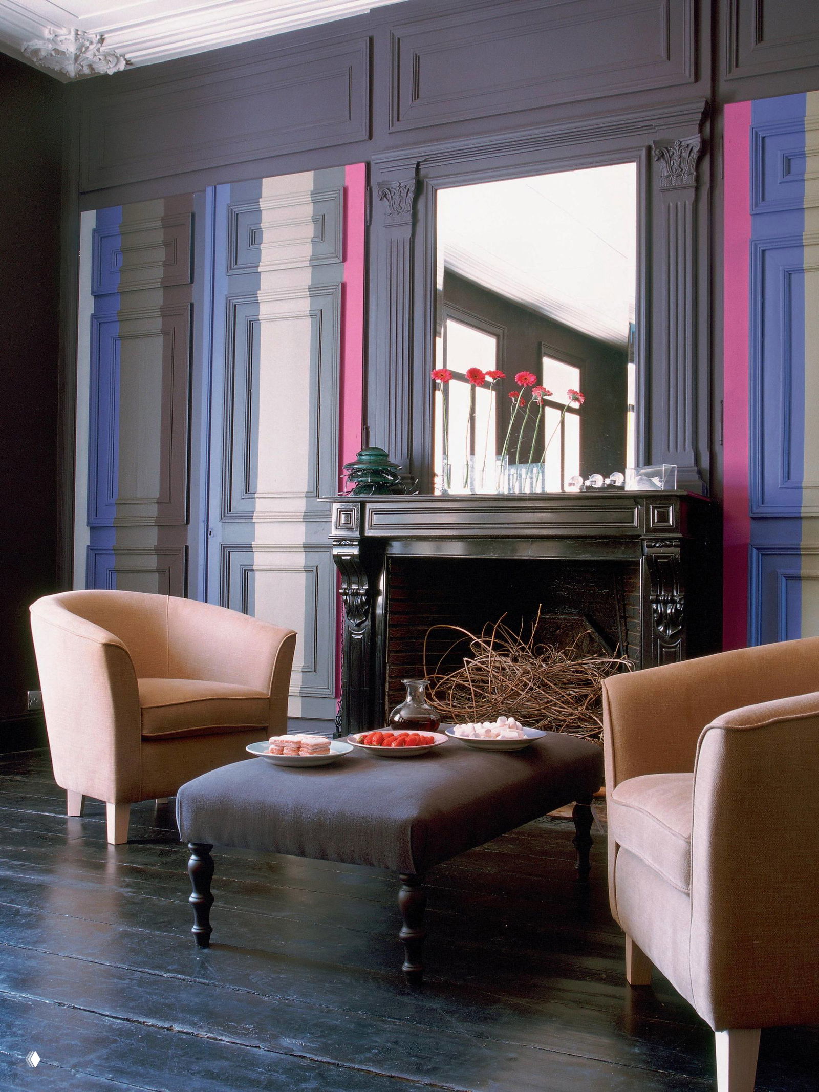 Классическая гостиная с декоративной каминной панелью, окрашенной в несколько тонов, мягкие кресла и столик перед камином создают уютный интерьер.