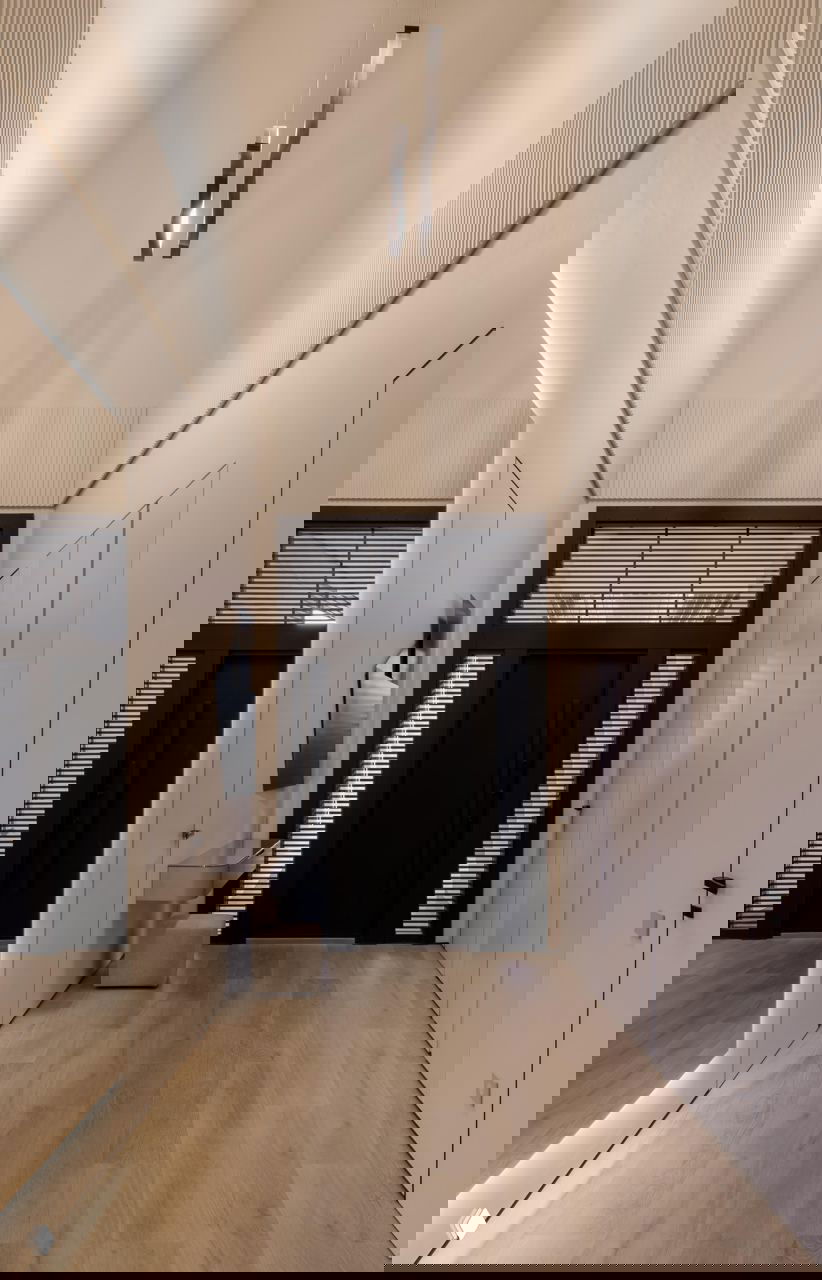 Прихожая с высокими потолками, зеркальной стеной и тёмной входной дверью, деревянный пол и мягкое равномерное освещение подчеркивают масштаб пространства.