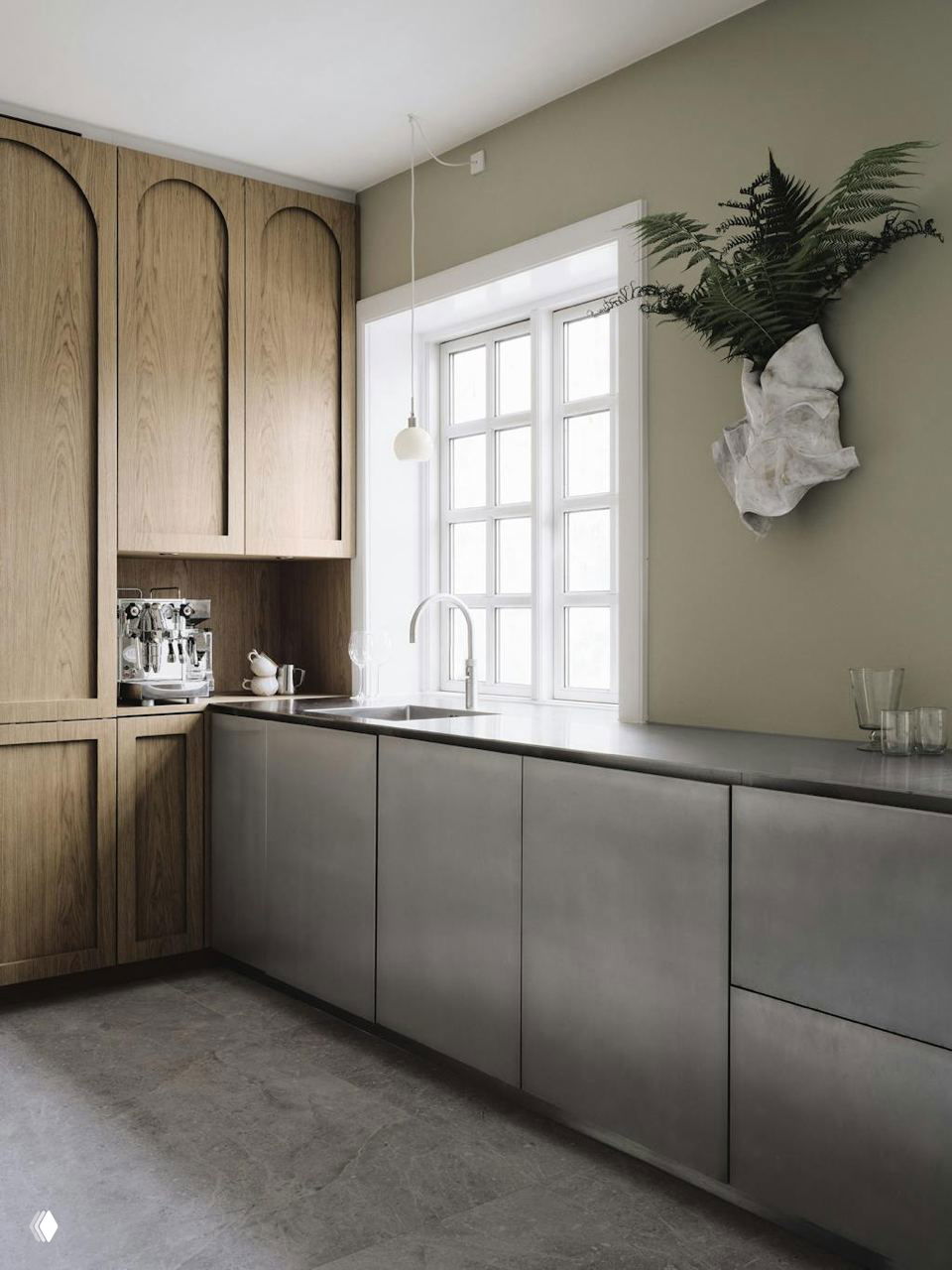 Кухонный интерьер с деревянными фасадами и матовой стальной столешницей у большого окна; акцентное растение на стене и нейтральная цветовая гамма.