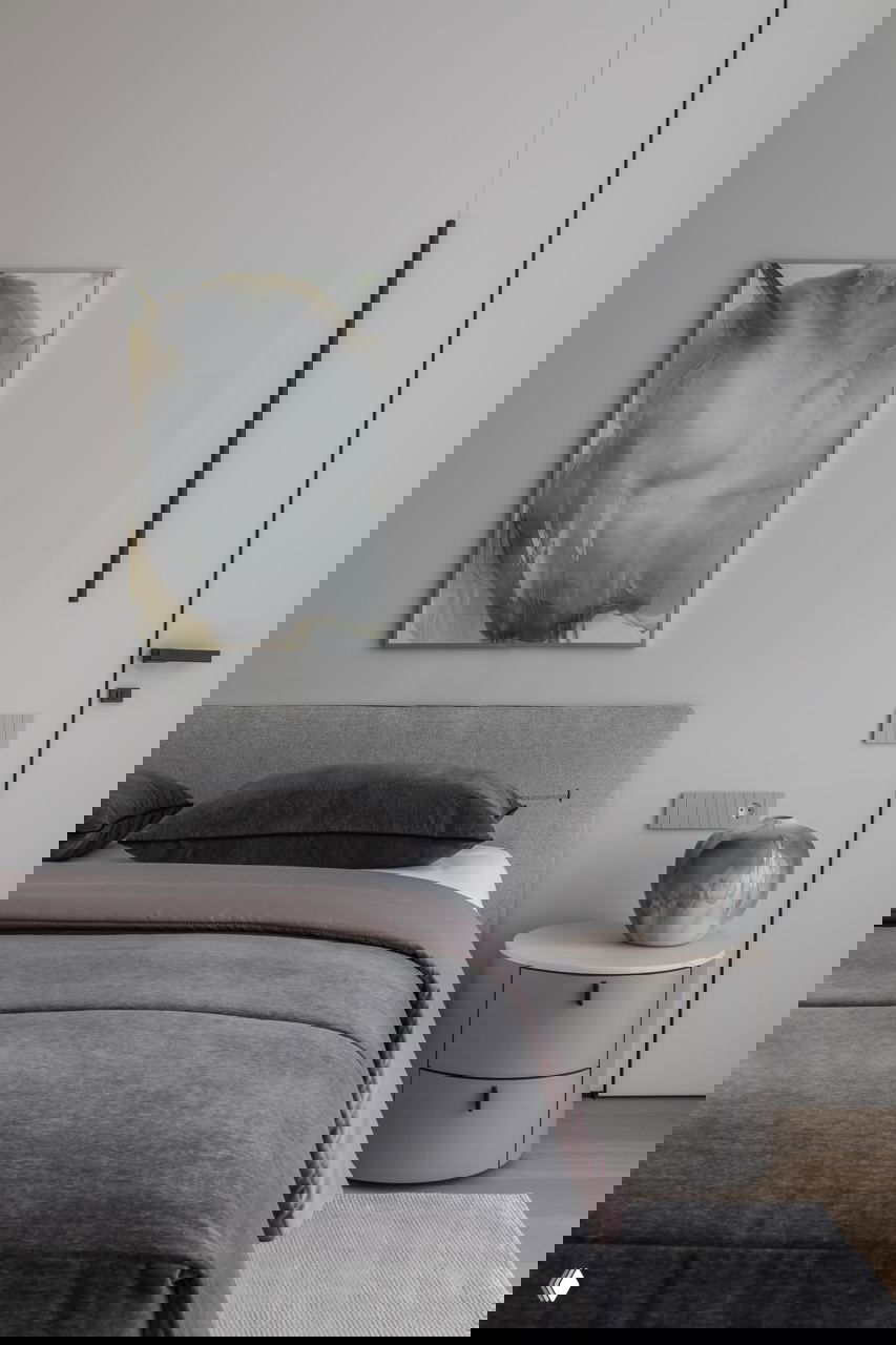 Спальня с серым изголовьем, мягким текстилем и абстрактной картиной на стене — спокойные нейтральные оттенки и минималистичные акценты.