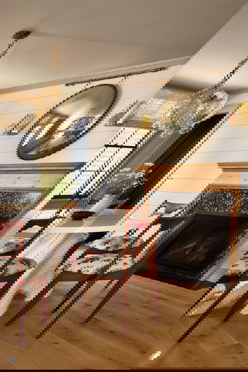 Столовая зона с белым круглым столом, деревянным камином и зеркалом в раме — сочетание светлых и тёмных акцентов в интерьере.