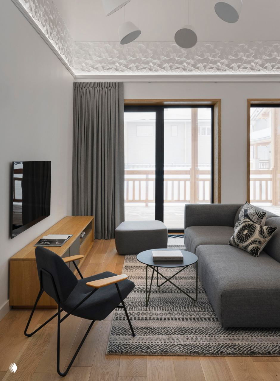 Уютная зона отдыха: серый модульный диван, кресло с деревянными подлокотниками, журнальный столик и декоративный ковёр в северной палитре.