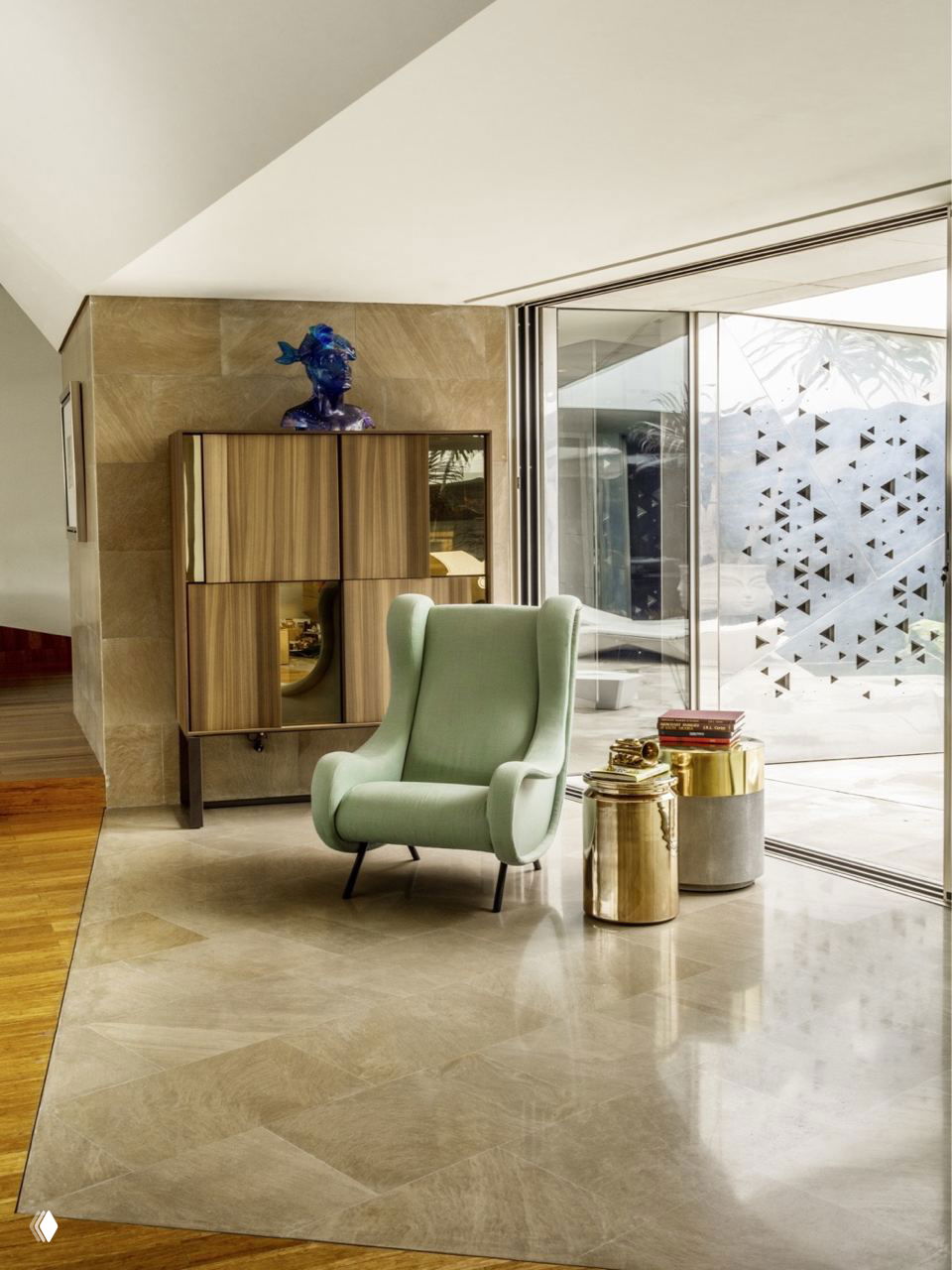 Угол с мягким светло-зеленым креслом, деревянным шкафом и панорамным остеклением; сочетание дерева, мрамора и металлических деталей в интерьере.