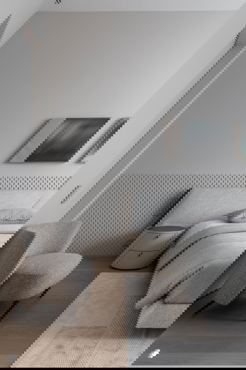 Ещё одна спальня с низкой кроватью, мягким креслом и рельефной стеновой панелью — интерьер в пастельных тонах и натуральных фактурах.