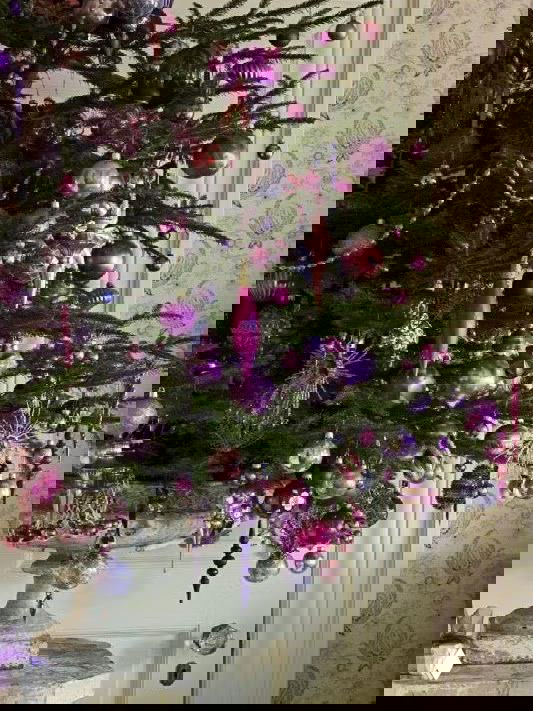 Тёмная ёлка в светлом помещении: проволочная корзина с тканевой подкладкой как основа, подарки и декоративная гирлянда на полу.