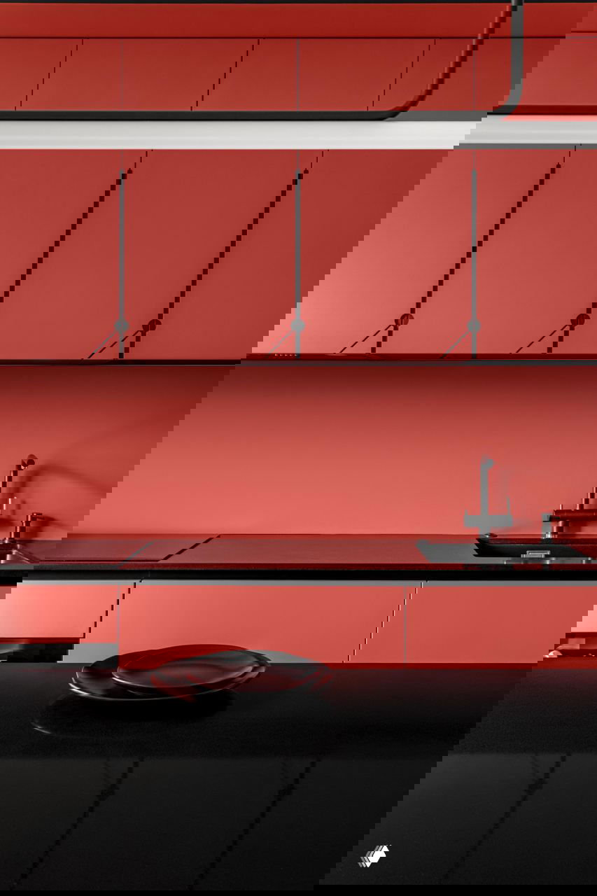 Крупный план кухни: ровные фасады кораллово-красного цвета, тёмная столешница и чёрный смеситель в строгом минималистском стиле.