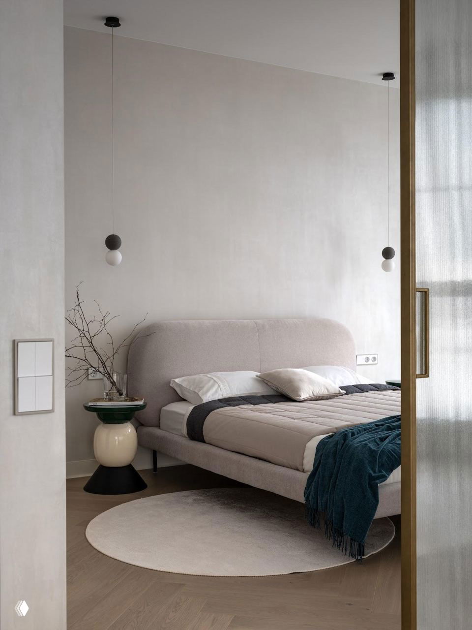 Спальня с округлым изголовьем кровати и круглым ковриком: пастельные тона, минималистичный прикроватный столик и спокойная атмосферная отделка.
