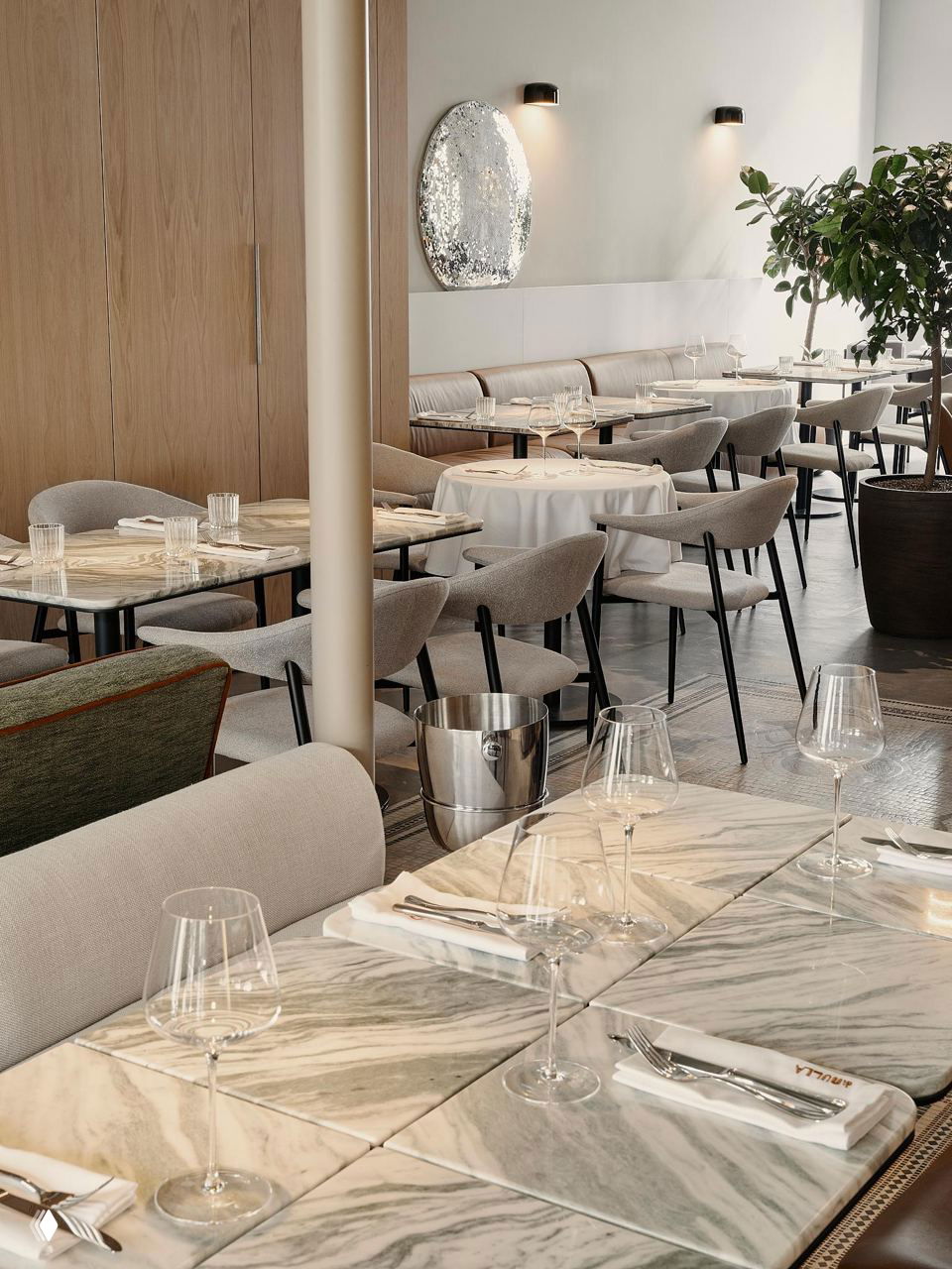 Интерьер кафе Di Nulla в Москве: мраморные столы, аккуратно расставленные бокалы и нейтральные стулья на фоне растений и мягкого света, ощущение лёгкости.