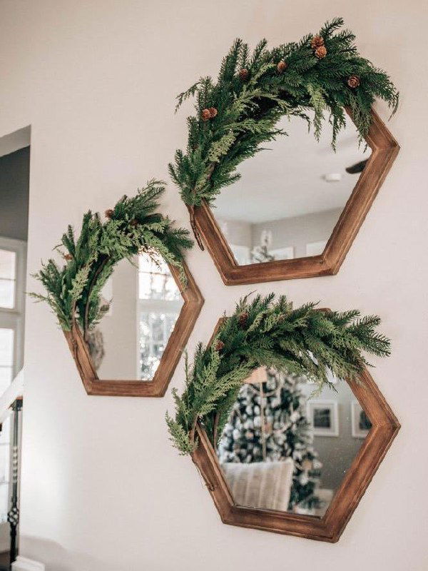Три шестиугольных зеркала, украшенные хвойными композициями и шишками — вариант декора стены с зеркальными акцентами и природными материалами.