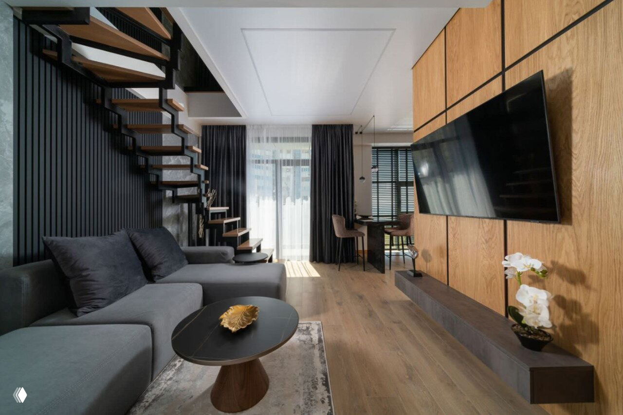 Интерьер гостиной 2-уровневой квартиры: современная зона отдыха с серым диваном, открытой лестницей и деревянной панелью для телевизора, стильный дизайн.
