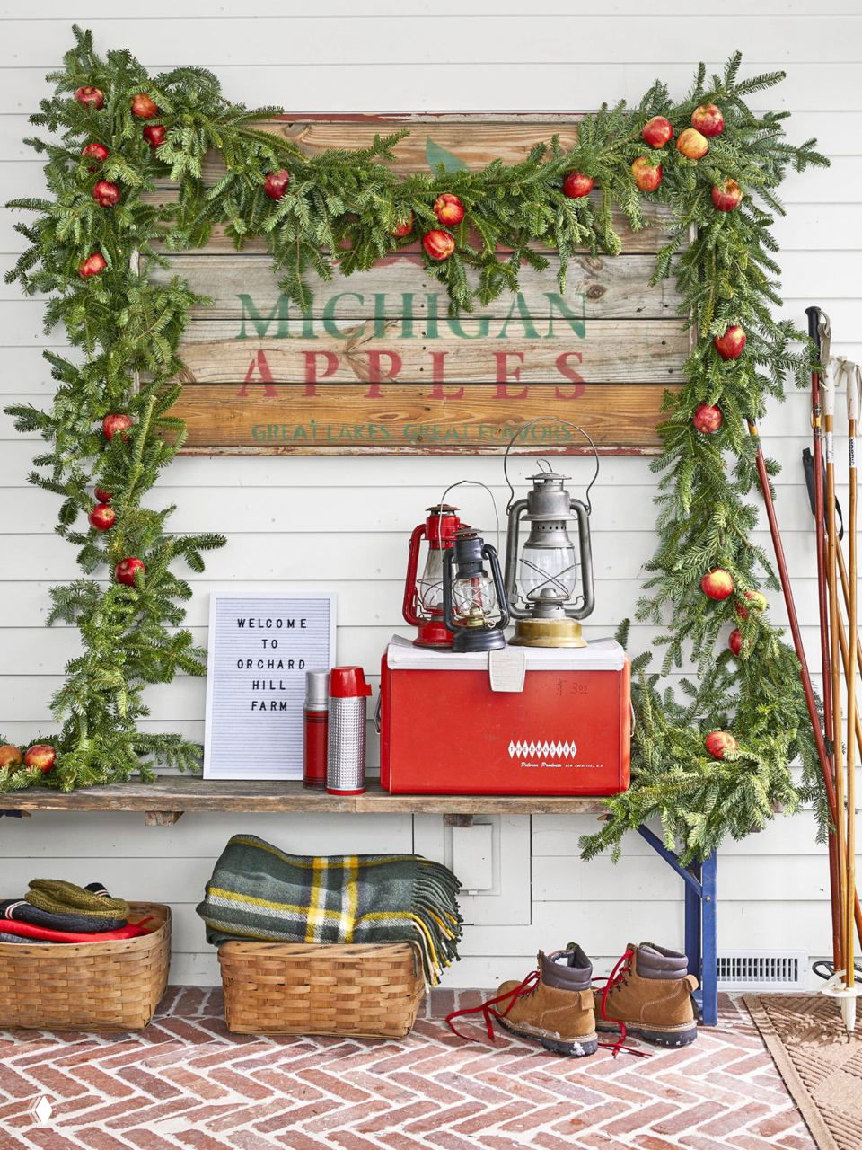 Декор в прихожей: зелёные гирлянды с красными яблоками, походная атмосфера и корзины у входа создают тёплый деревенский образ.