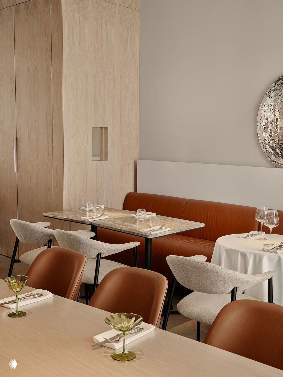 Уголок заведения с кожаным банкетом и светлыми деревянными панелями, смешение текстур и форм, характерное для проекта DA Bureau в кафе Di Nulla.