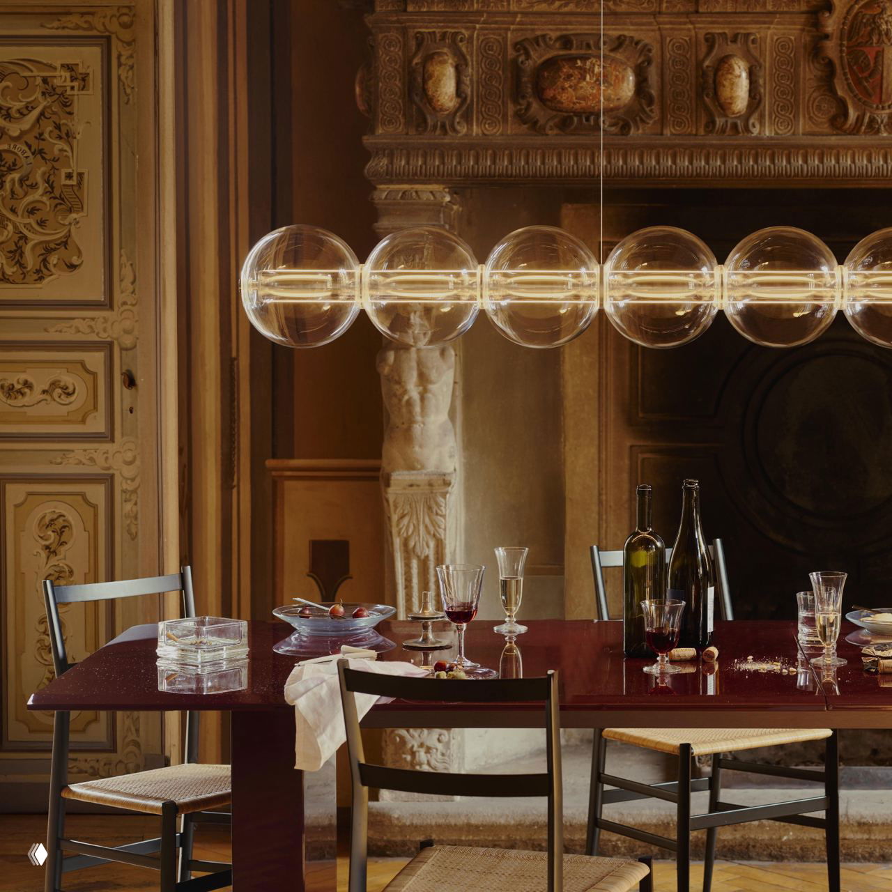 Ряд прозрачных стеклянных шаров Luce Sferica на алюминиевой оси, тёплое рассеянное освещение над обеденным столом в классическом интерьере.