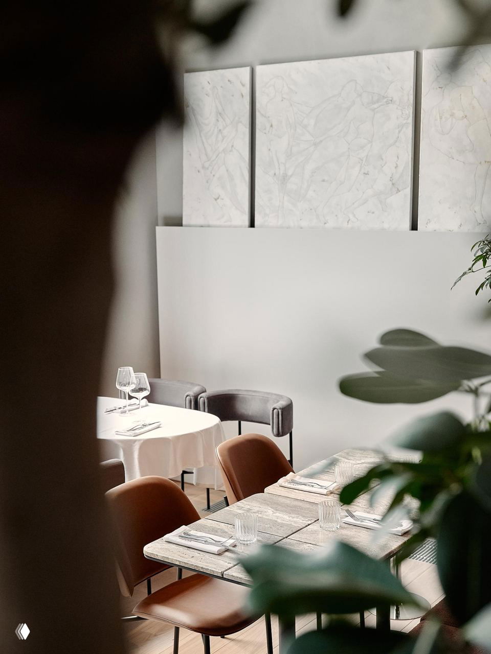 Вид через зелёные листья на столы с мраморными плитами и мягкими креслами, акцент на естественные материалы и «контролируемый хаос» в планировке.