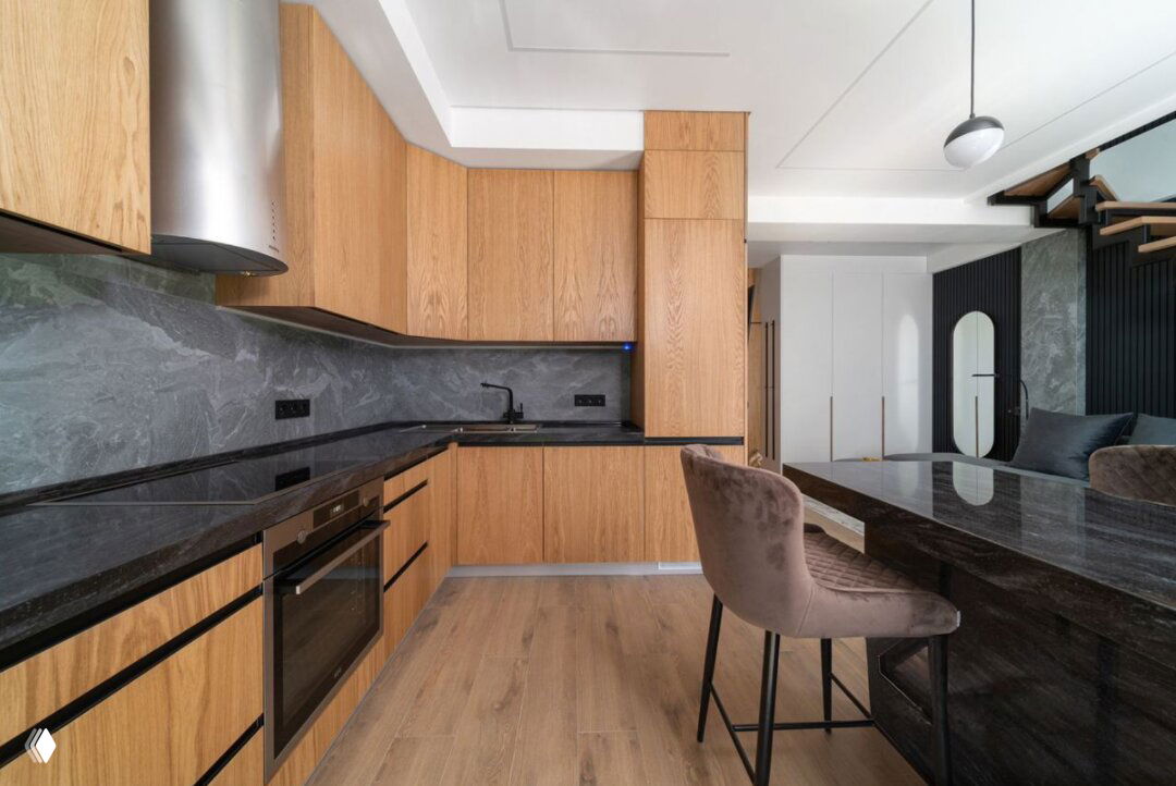 Кухонная зона с деревянными фасадами и чёрной столешницей в квартире ЖК Фестивальный: встроенная техника и обеденная стойка в открытой планировке.