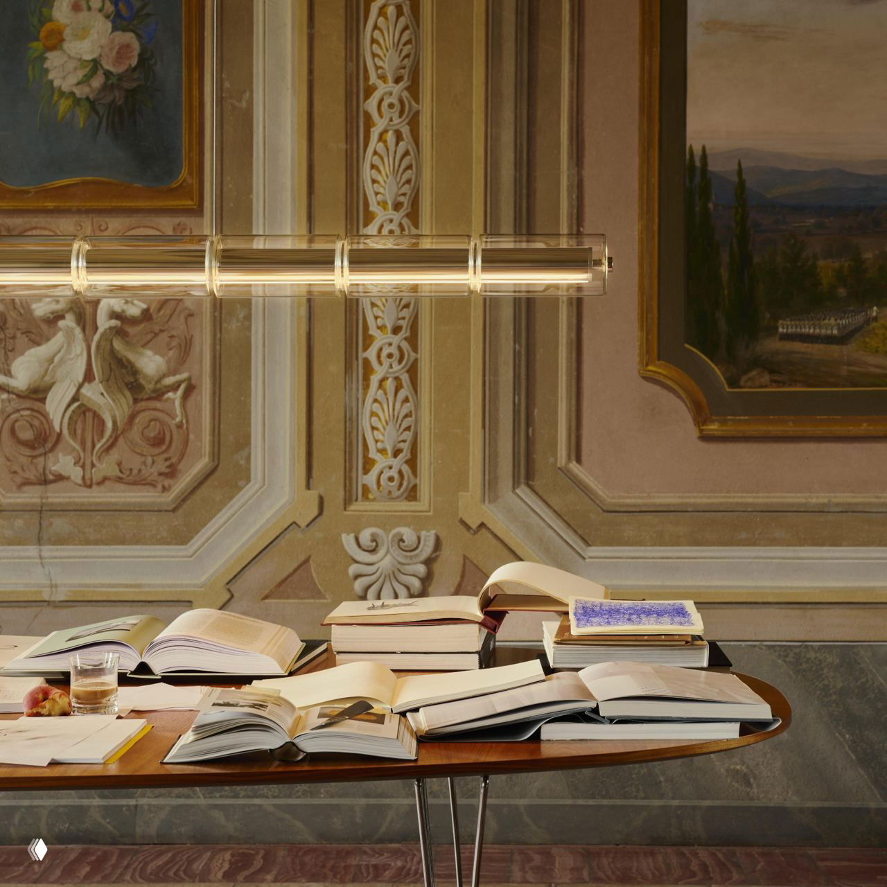 Стол с раскрытыми книгами и длинный линейный модуль светильника на фоне расписного музейного интерьера, атмосферная презентация объекта.
