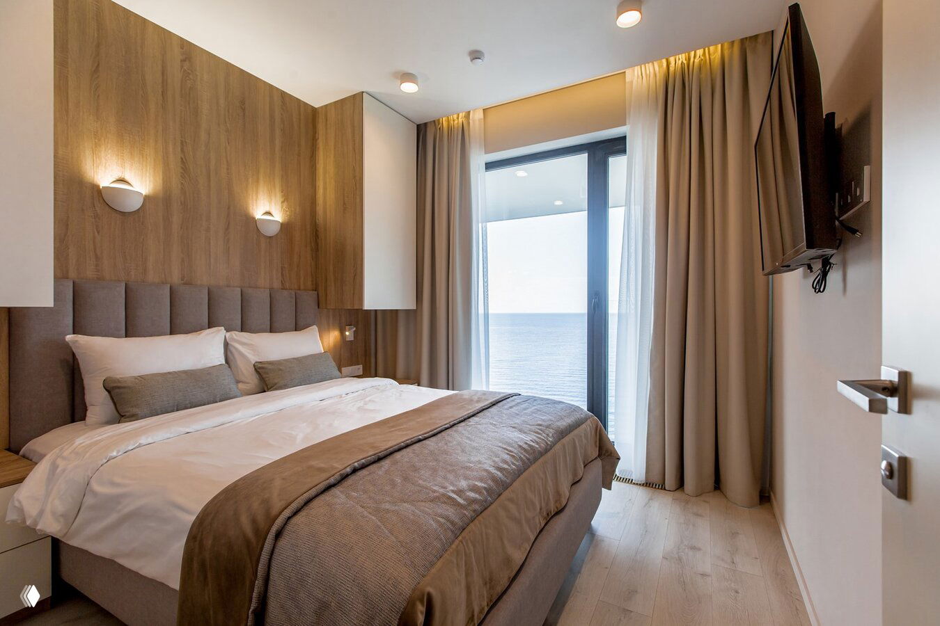 Спальня с большой кроватью и панорамным окном с видом на море: светлый интерьер, шторы и балкон в жилом комплексе на берегу Сочи.