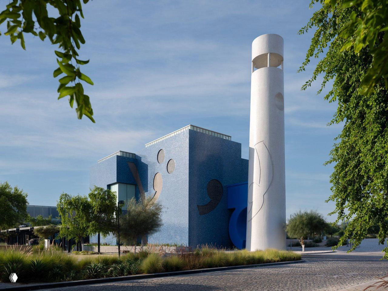 Утренний вид на музей Хусейна в Дохе: минималистичная голубая масса здания, окружённая зеленью и мощёной площадью у входа.