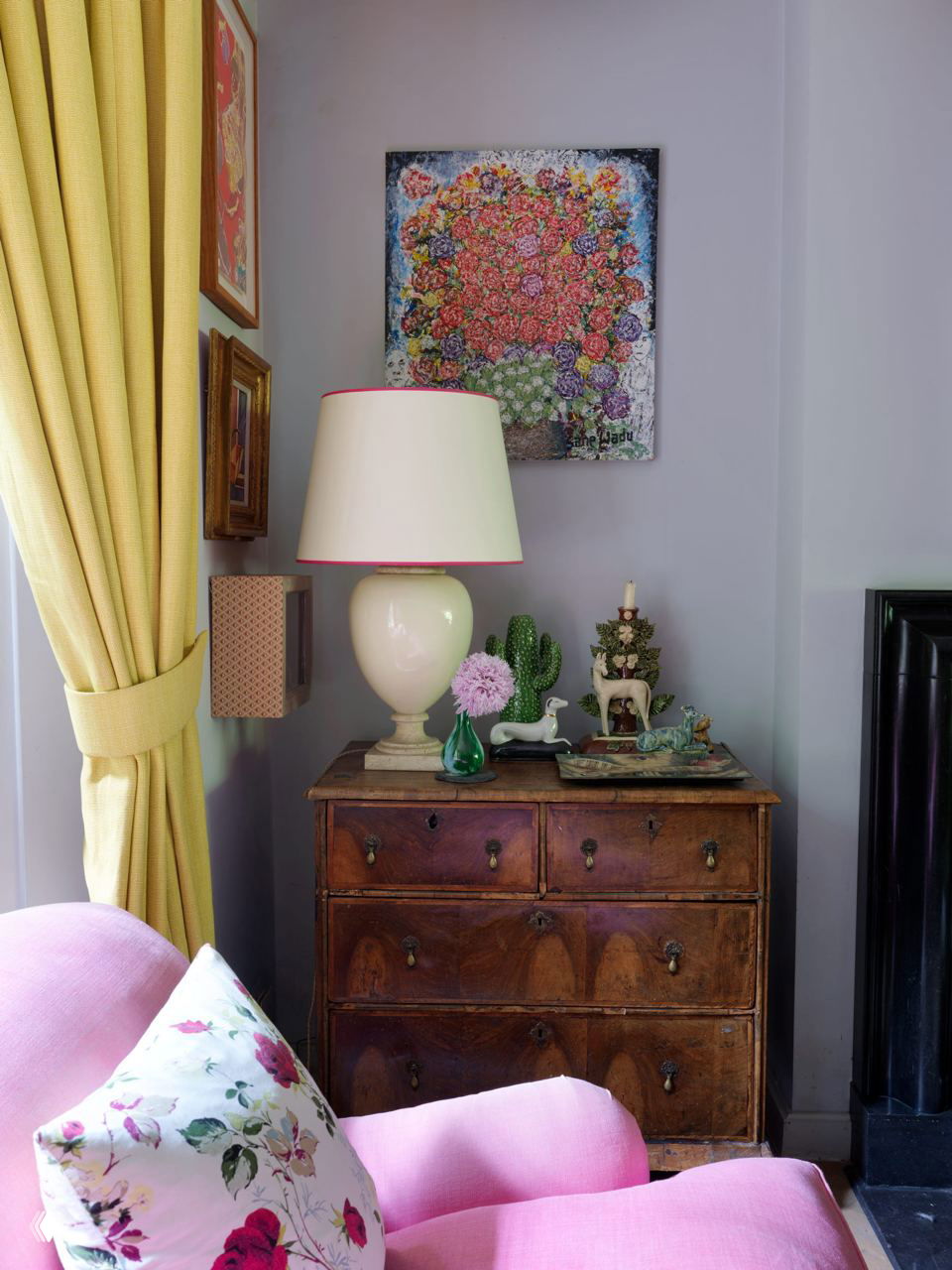 Уютный уголок с старинным комодом, керамической лампой, желтыми шторами и розовым креслом с цветной подушкой — винтажные и яркие акценты в доме.