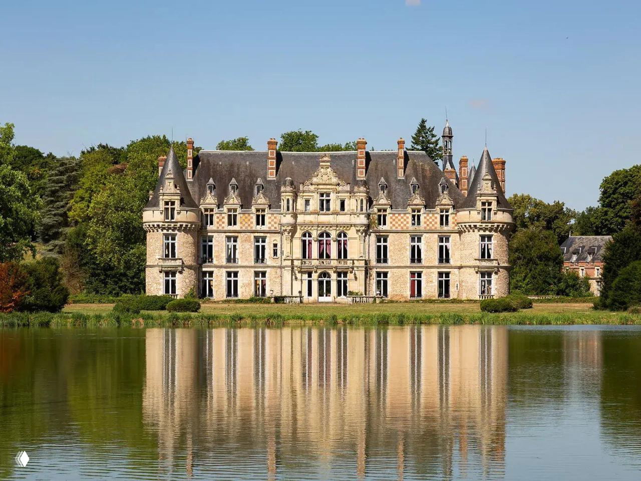 Фасад замка Эсклимон XVI века с зеркальным отражением в пруду: центральный корпус, башенки, каменная отделка и окружающий парк.